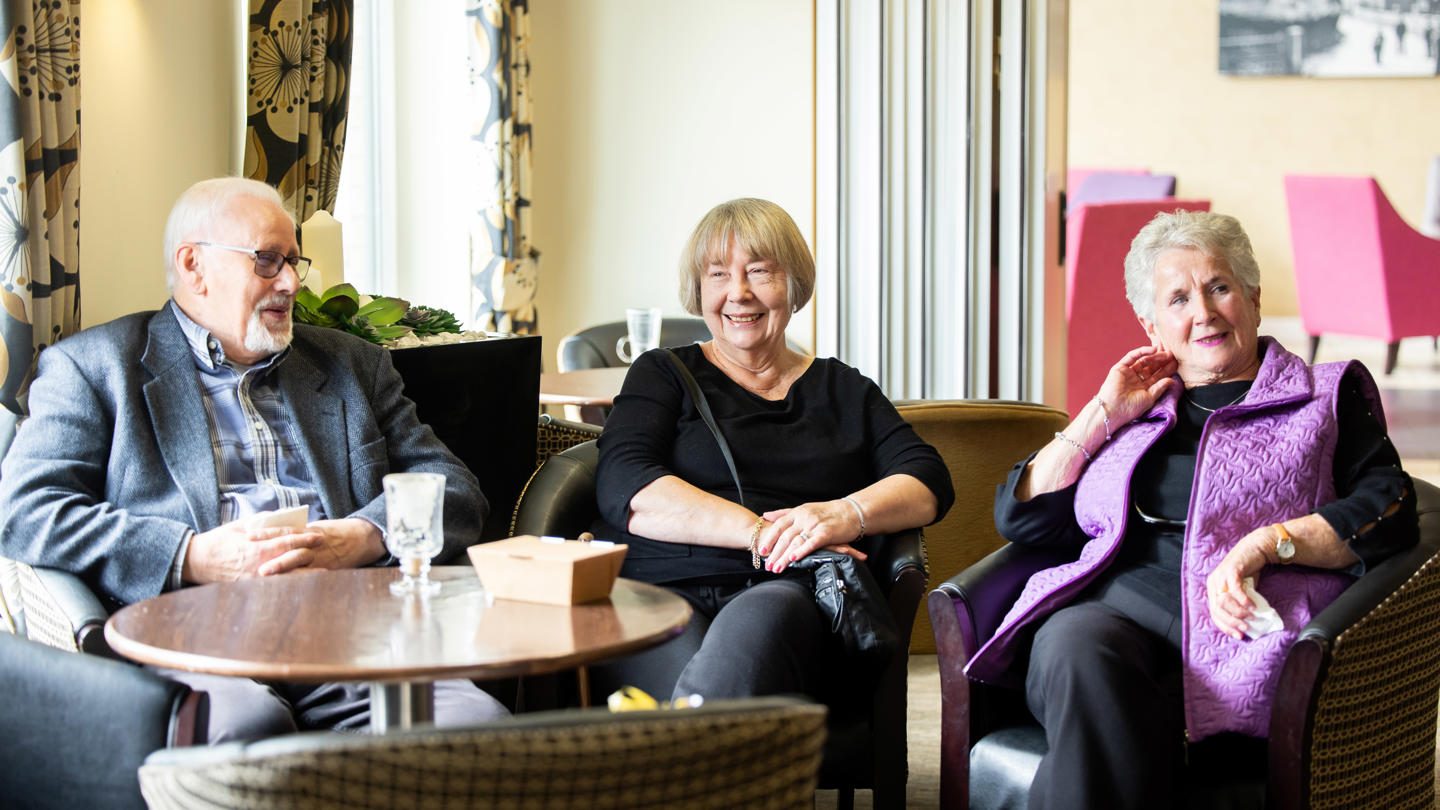 Three older people sat in a row in a relaxed dining room setting. 
